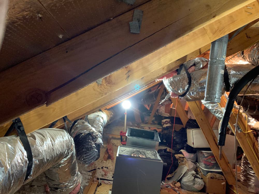 Attic view with insulation, ductwork, and a work light illuminating the space.