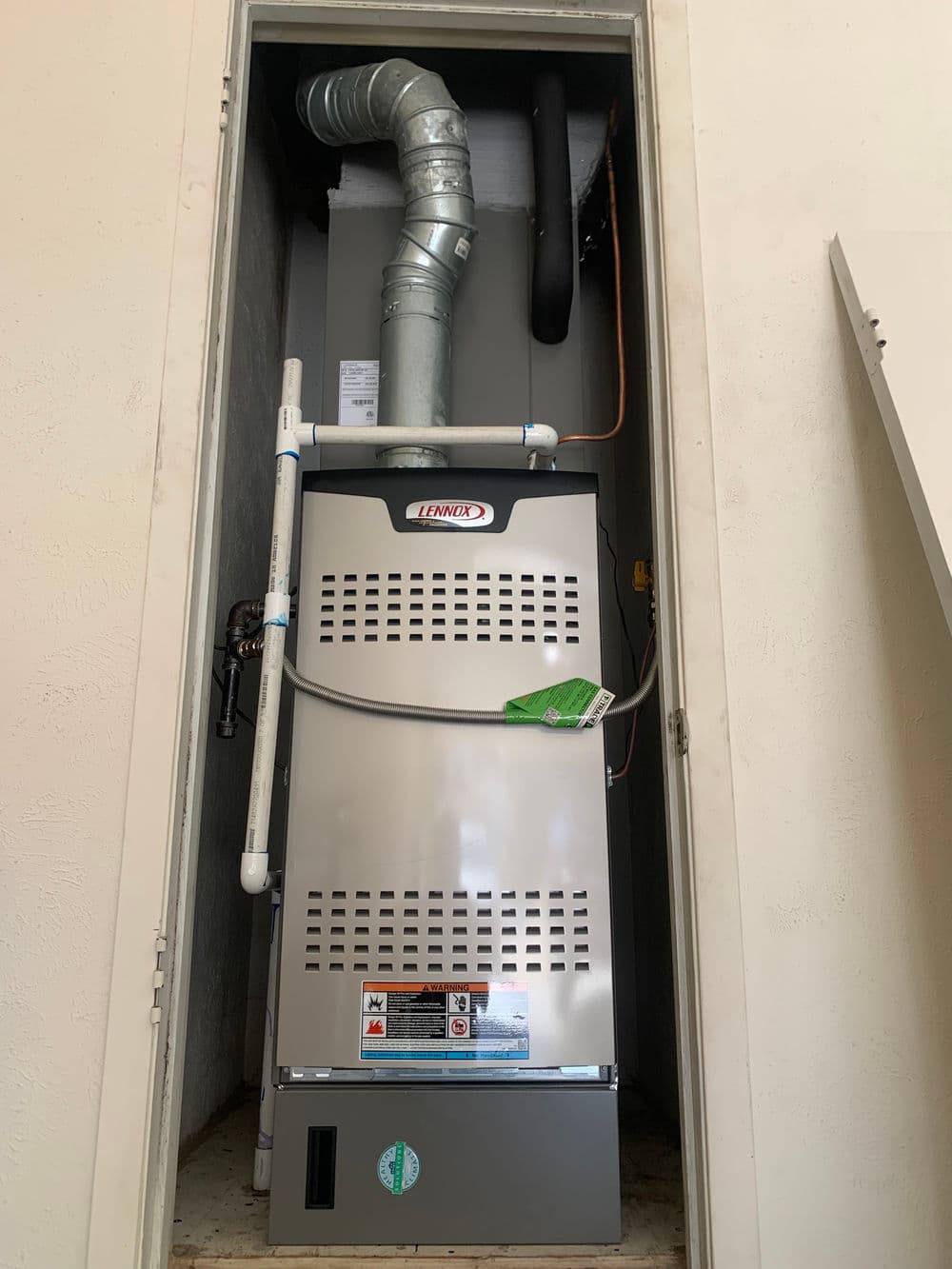 New Lennox furnace installed in a closet, featuring a metal exhaust pipe and ventilation system.