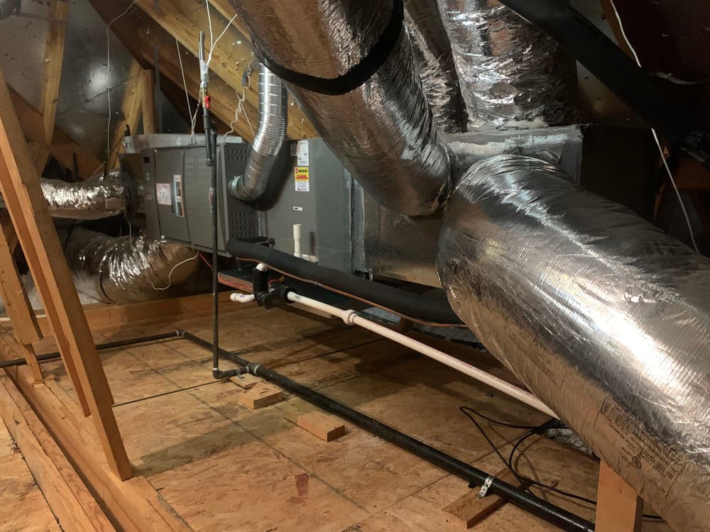 Attic heating system with ductwork and pipes, featuring insulated metal ducts.